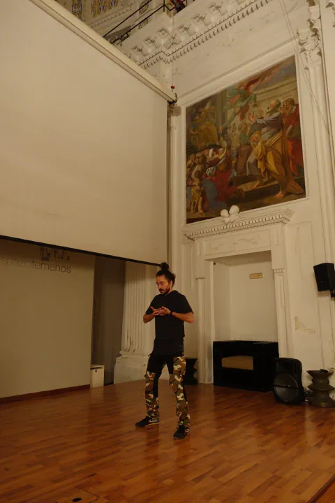 Oscar Gallo durante una lezione, in piedi al centro di una sala storica dal soffitto alto e affrescato.